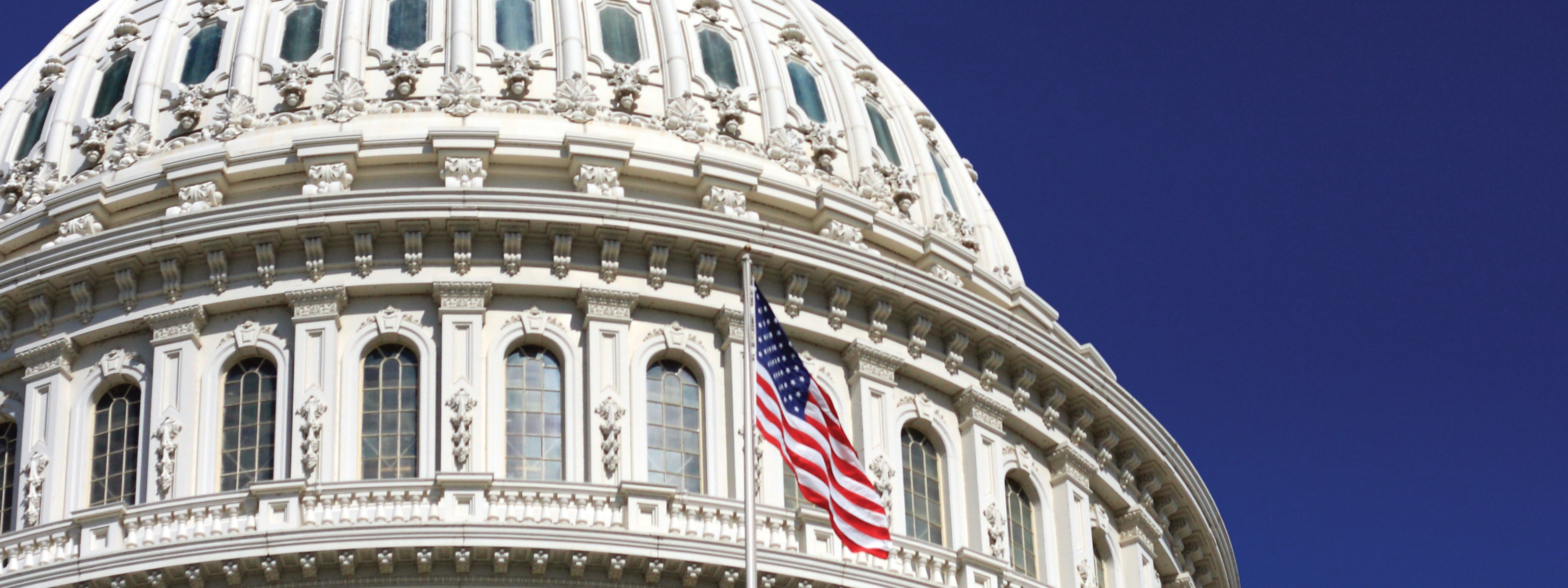 Close up of the U.S. Capitol with a dark blue sky in the background and a U.S. flag in the foreground 